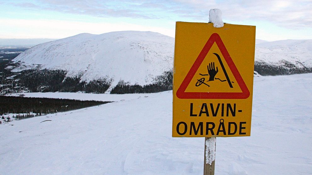 Skylt vid snötäckt berg varnar för lavinområde.