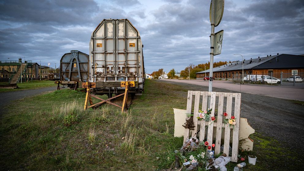 Lastbilstrailer vid väg. Minnesplats med blommor framför vägmärke. Cloudy sky.