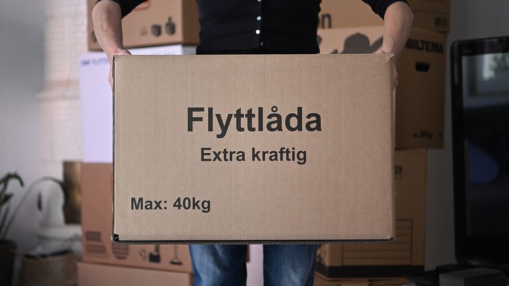 En person fotograferad från brösthöjd och ner håller en stor flyttkartong framför sig.