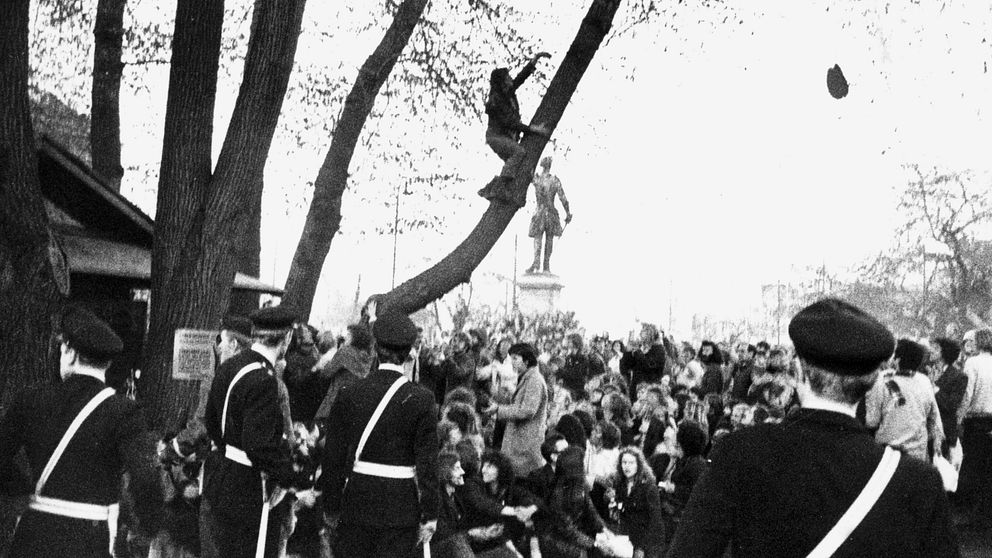Bild från Kungsträdgården under Almstriden 1971. Svartvitt foto med poliser i förgrunden och demonstranter i träden.