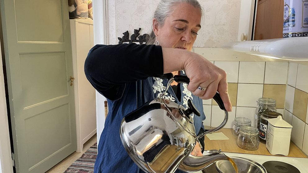 Person häller vatten från en kanna i kök. Kaklat vägg och glasburkar syns i bakgrunden.