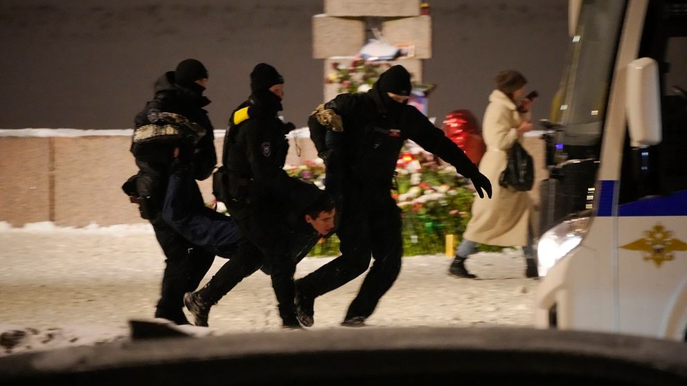 Tre poliser griper en man och lyfter honom mot en polisbil vid minnesmonument i Sankt Petersburg