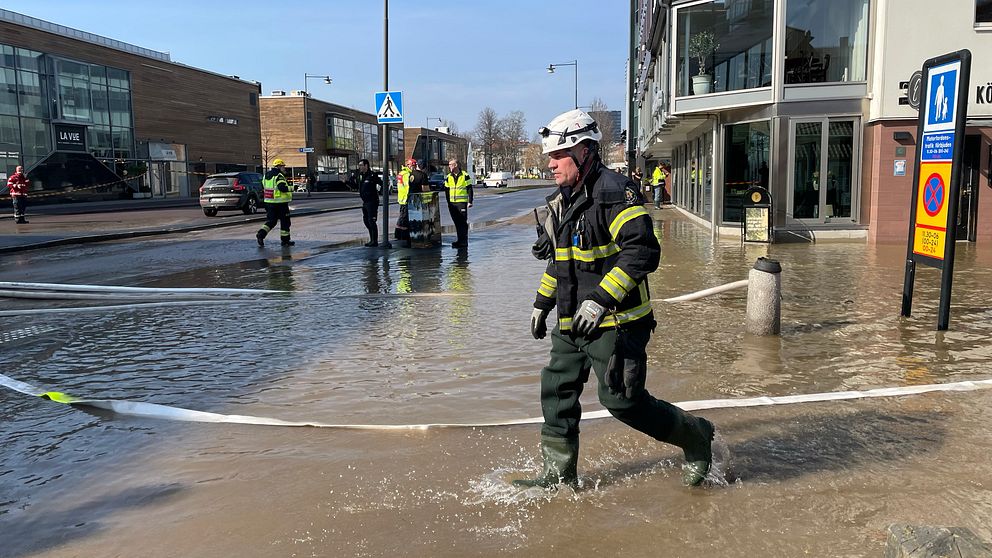 Brandmän jobbar på en översvämmad gata i stadsmiljö.