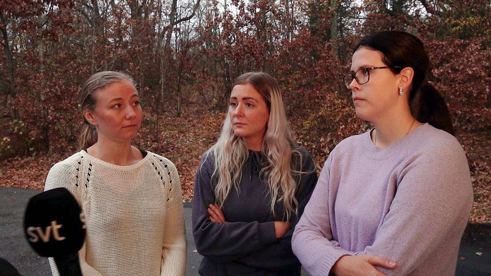 Tre kvinnor står utomhus i en skogsaktig miljö med höstfärger. De har armarna i kors och ser allvarliga ut. En mikrofon med texten ”svt” är synlig i förgrunden.