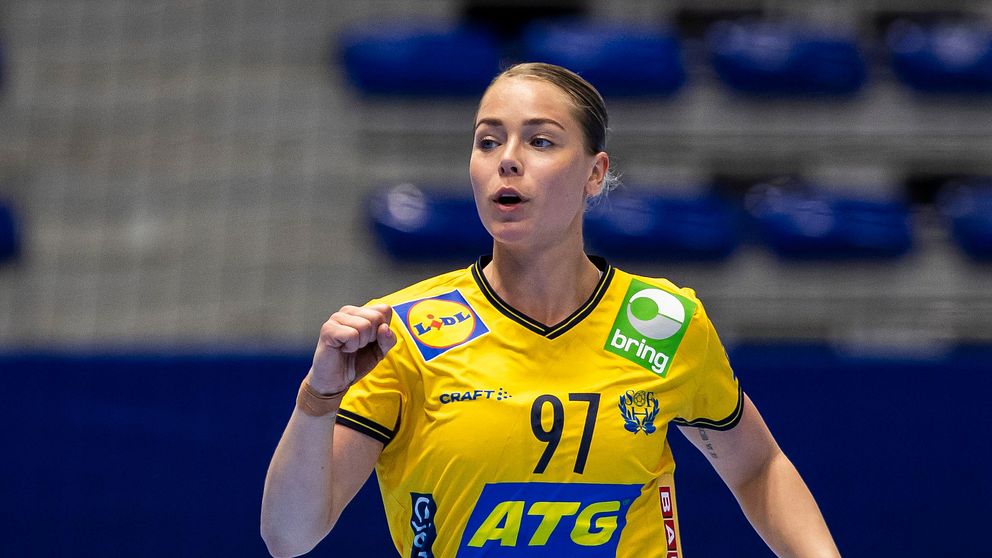 Handbollsspelare i gul tröja springer på plan. Tomma sittplatser i bakgrunden.