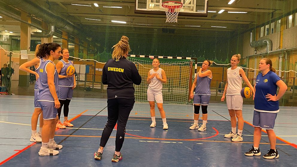 En grupp kvinnliga basketspelare genomgår träning i en sporthall.