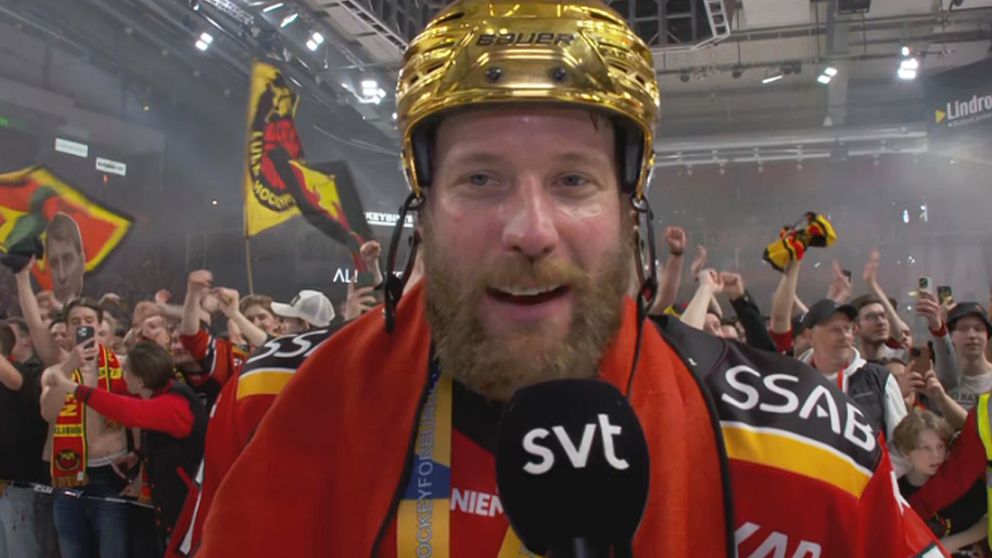 Hockeystjärna med guldhjälm intervjuas på isen, fans firar i bakgrunden.