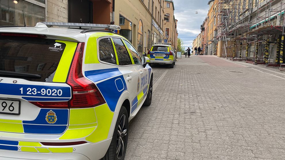 Två polisbilar parkerade längs en tom gata mellan hus i stadsmiljö.