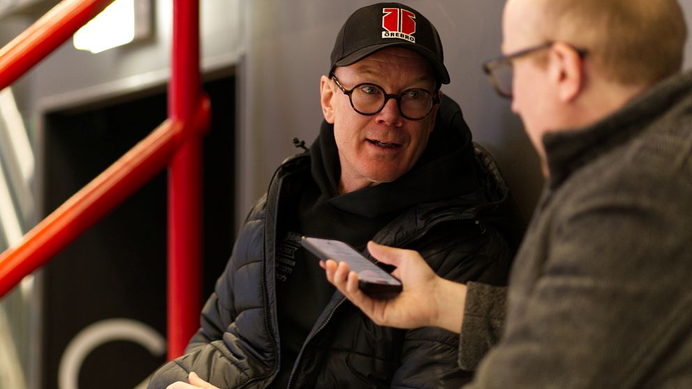 Niklas Eriksson i glasögon blir intervjuad av en journalist med mobiltelefon.