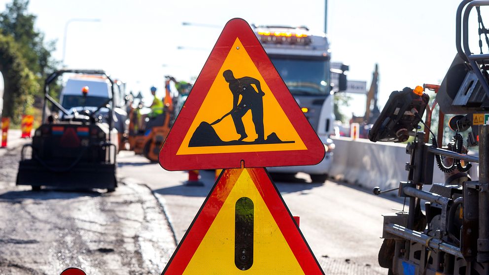 Vägarbete pågår. Varningsskyltar och maskiner syns på en trafikerad väg.