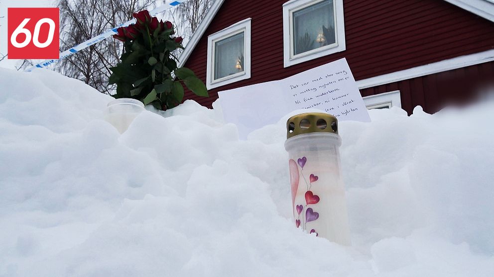 Snö framför en röd träbyggnad med ett tänt gravljus, en bukett rosor och ett handskrivet brev.