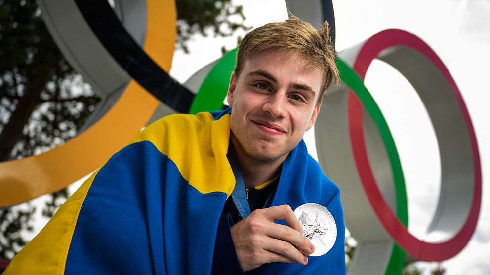 Bordtennisstjärnan Truls Möregårdh med sin olympiska silvermedalj om halsen och svenska flaggan om ryggen.