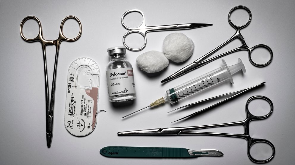 Sektionsvis arrangemang av medicinska instrument och material, inklusive operationssaxar, en spruta, en flaska med Xylocain, en skalpell, och två bomullsrondeller.