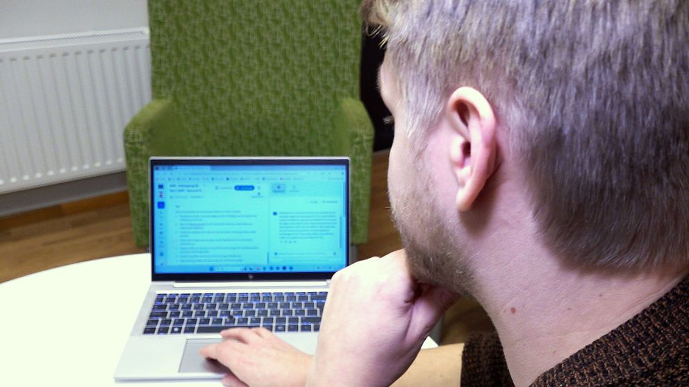 Socialsekreteraren Oscar Lundström använder en bärbar dator i ett rum med grön fåtölj i bakgrunden.