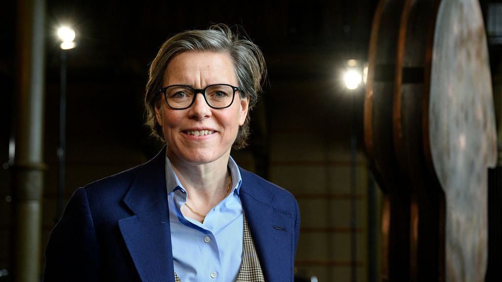 Kvinna i kostym framför industriell bakgrund.