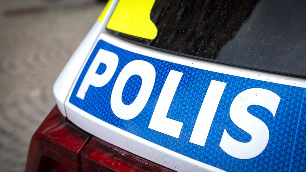 Närbild av en svensk polisbil som visar texten ”POLIS” på baksidan, med en blå bakgrund och reflekterande motiv.