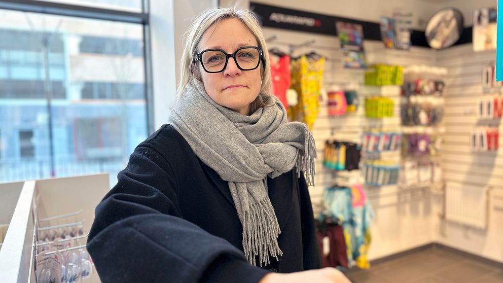 Badhuschef Åsa Säfsten Boman från Umeå kommun i vinterkläder står vid en butikshylla med simdräkter och andra produkter på bakre väggen.