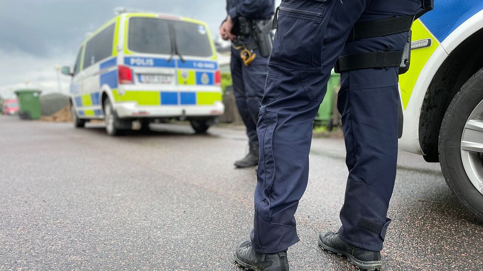 Två poliser står vid polisbil och polisfordon på asfalterad gata.