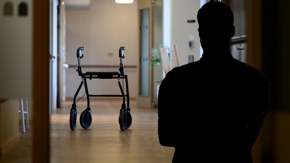 En person i siluett i en sjukhuskorridor med en tom rollator i bakgrunden.