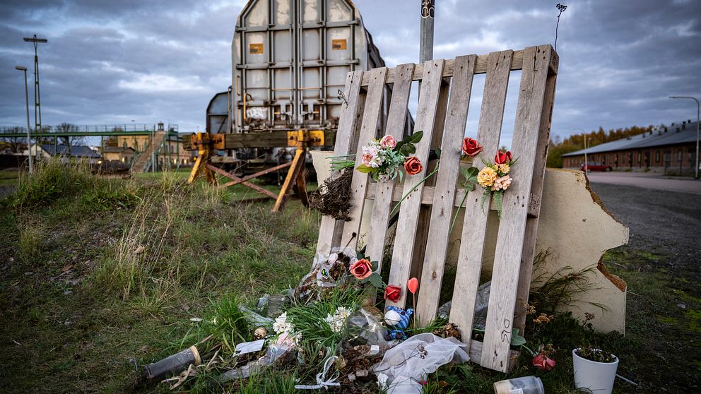 Minnesplats vid järnväg med blommor och ljus, gammalt tåg i bakgrunden.