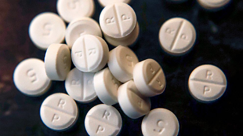 Vit medicin i form av tabletter spridda ut på en mörk yta, med vissa tabletter märkta med siffran 5 och bokstaven R samt P.