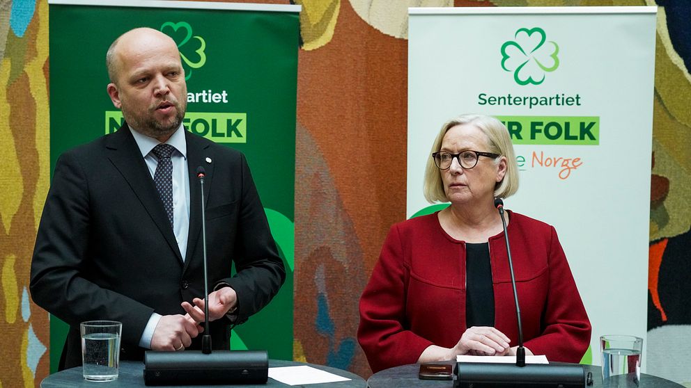 Två personer står vid podier med mikrofoner framför affischer från Senterpartiet i Norge.