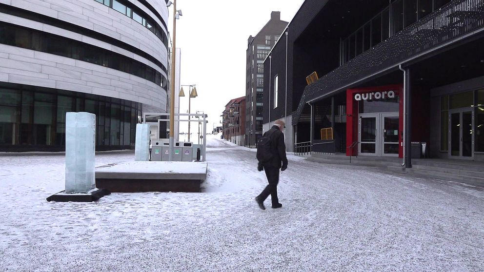 En man går genom en snötäckt gata mellan moderna byggnader.