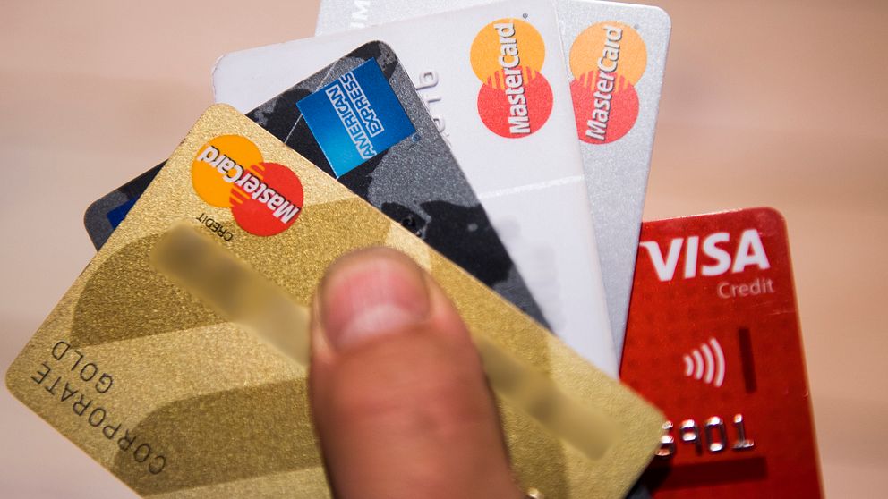 En hand håller flera kreditkort från Mastercard och Visa.