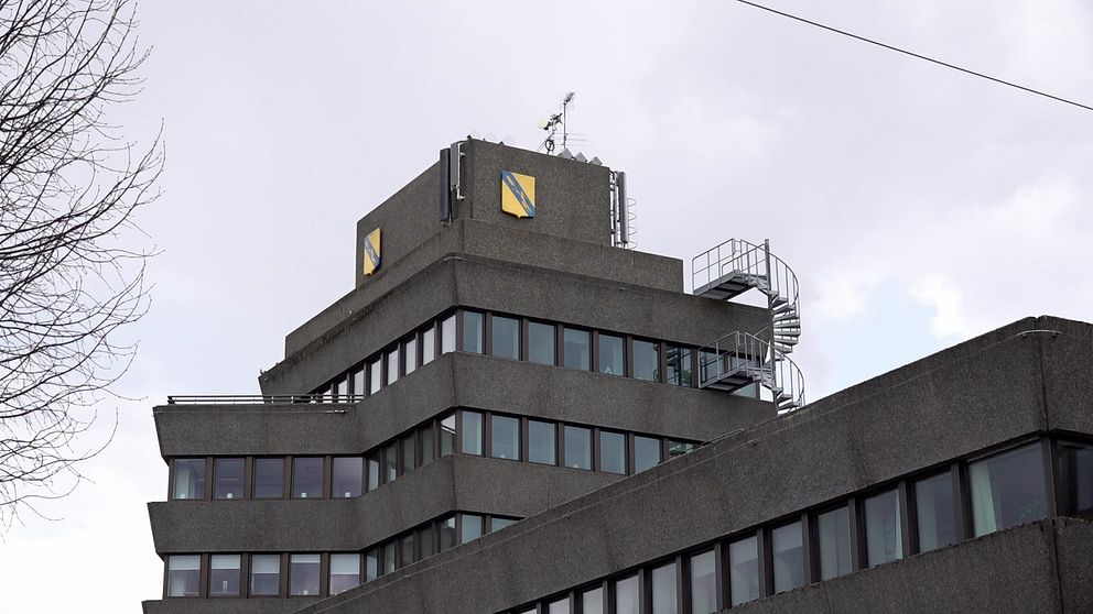 Grå kontorsbyggnad med spiraltrappa utvändigt och gula kommunlogotyper på toppen.
