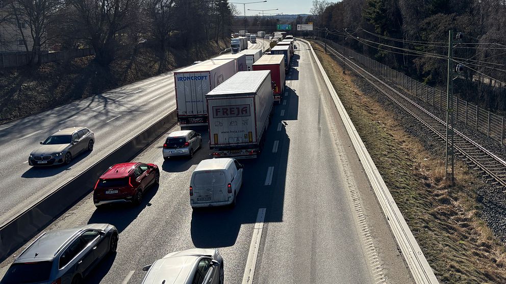 Trafikstockning på motorväg vid sidan av järnvägsspår, kvarstående vinterträd.