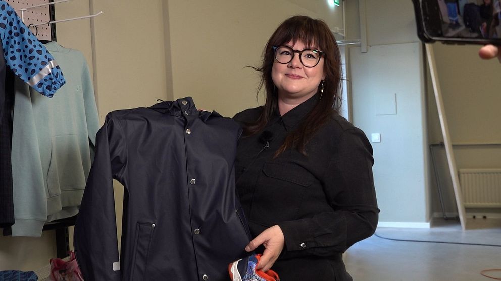 Butikschefen Kajsa Johansson håller upp ett par skor och en regnjacka i den nya klädbutiken Klädrätt, i Rannebergen, som är en butik där ekonomiskt utsatta får tillgång att handla nya kläder för ett billigt pris.