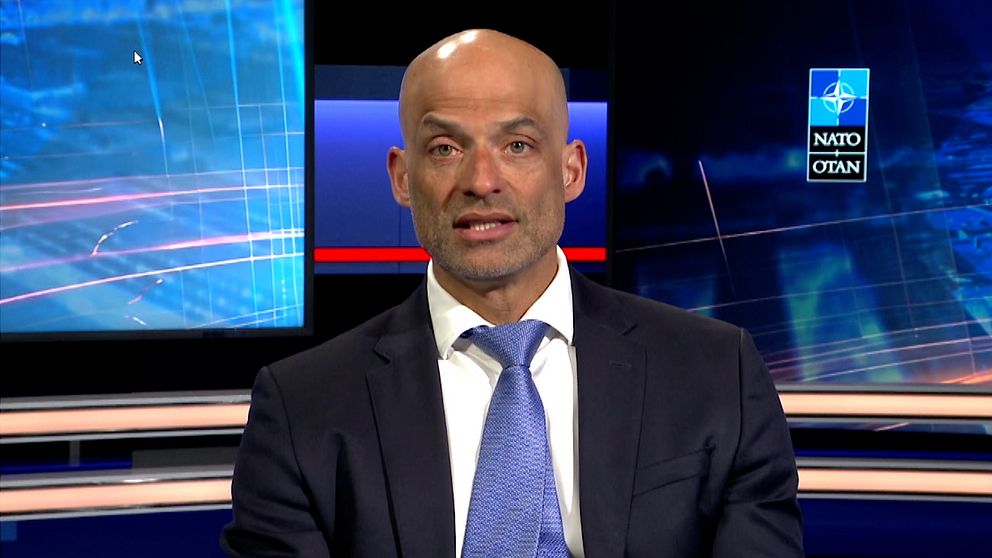 Person i kostym i tv-studio med blå bakgrund.