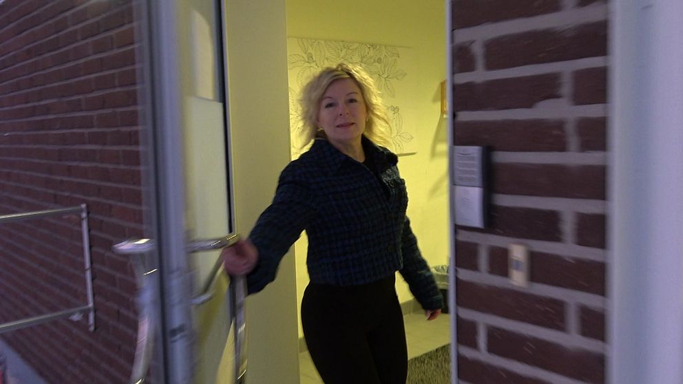 En person med ljus lockigt hår öppnar dörren till en byggnad med tegelväggar.