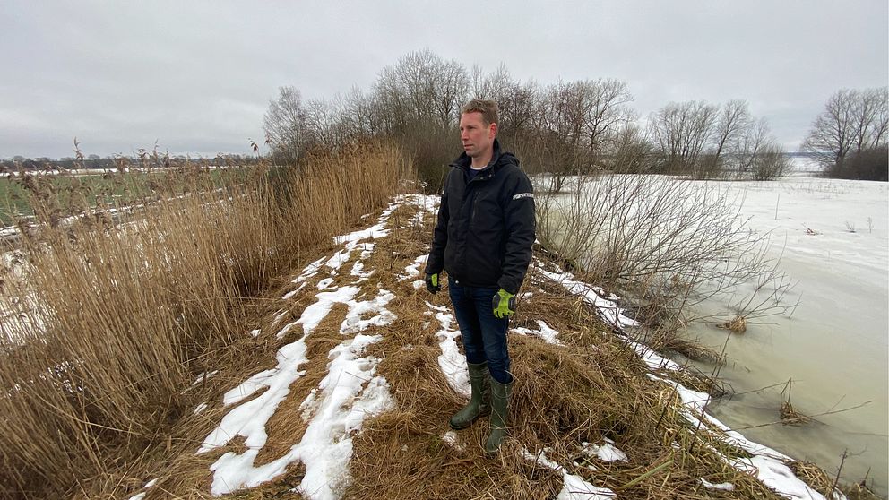 bild på man som står på en höjd mellan åkermark och en fryst sjö.