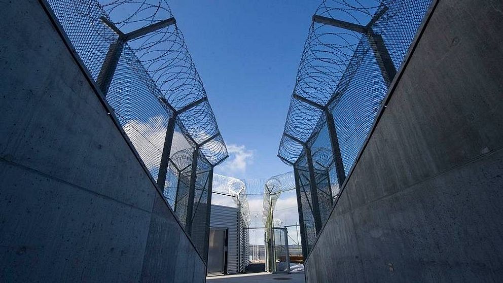 Fängelsemurar i betong med stängsel och taggtråd.