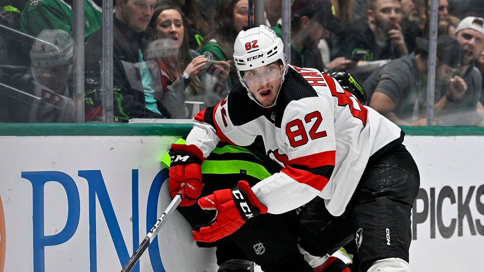 Ishockeyspelare från New Jersey Devils strider om pucken intill sargen under match.