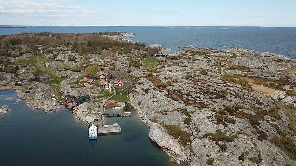 Flygbild av en skärgårdsö med hus, brygga och omgivande hav.