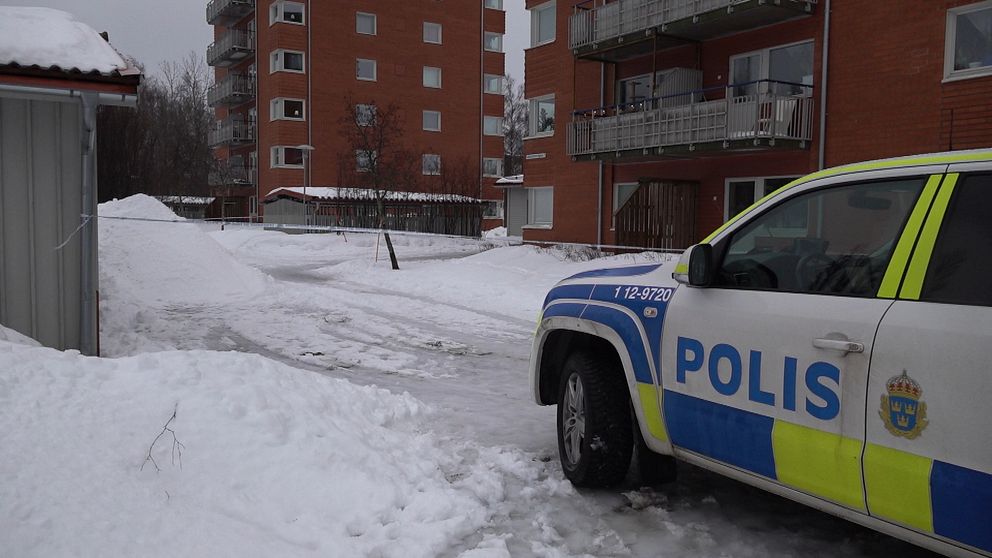 En polisbil parkerad i ett snötäckt bostadsområde med flerfamiljshus i bakgrunden.