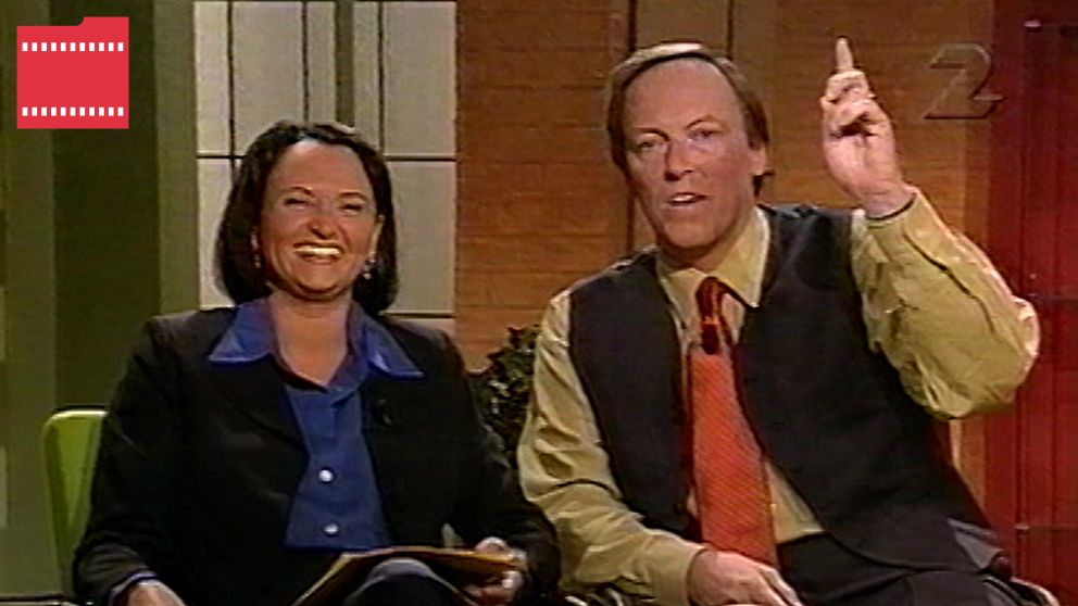 Två personer sitter i en studio, en av dem håller upp ett finger och verkar tala.