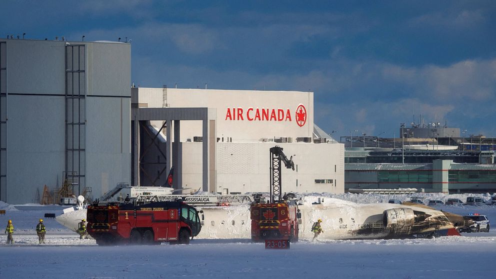 Räddningsfordon vid ett flygplansvrak framför Air Canadas hangar i vintrigt landskap.