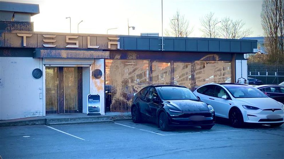 Två Tesla-bilar parkerade framför en Tesla-butik som är nersprutad med orange färg.