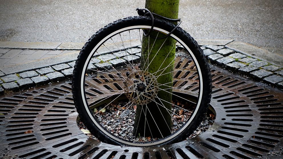 Ensamt cykelhjul fastlåst vid en stolpe på trottoaren.