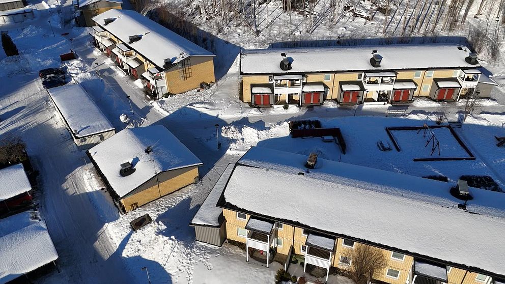 Flygbild över snötäckt bostadsområde med radhus och snöiga gångvägar.