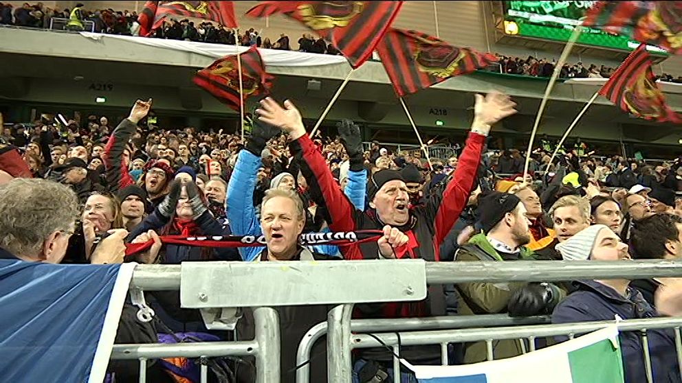 Fotbollsfans hejar och viftar med flaggor på en läktare.