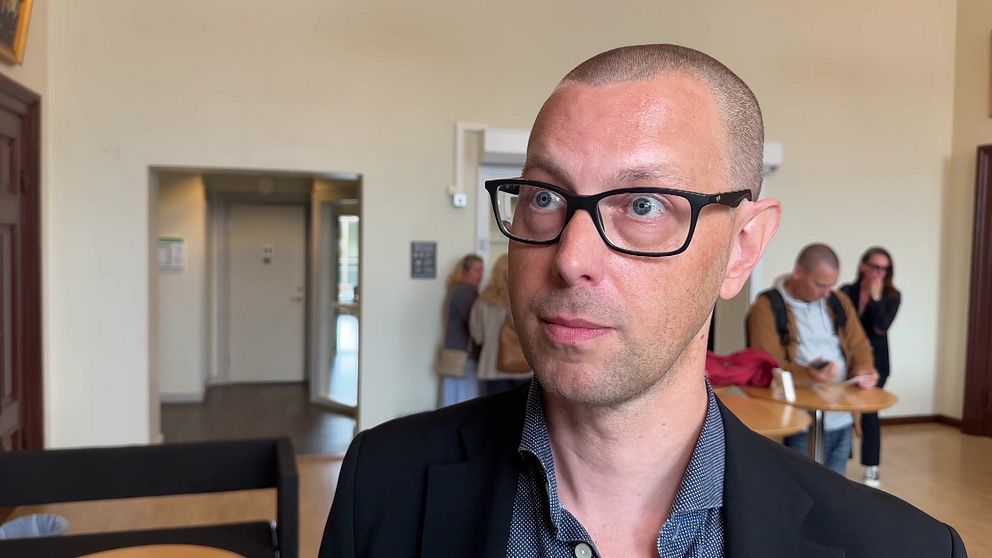 En person i en svart kavaj står i förgrunden, medan människor syns i bakgrunden inne i Värmlands tingsrätt.