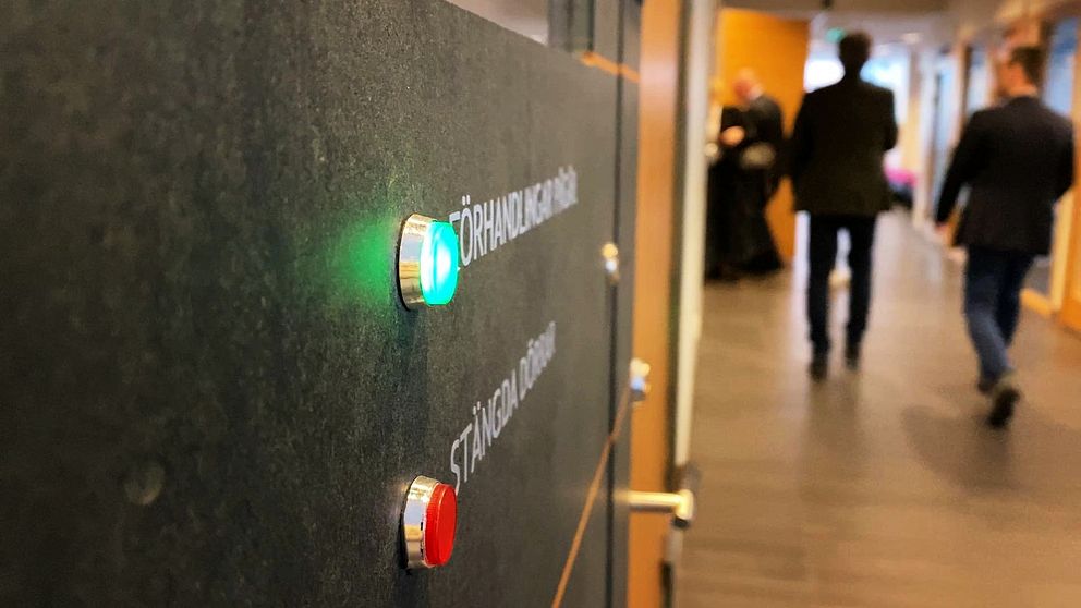 Personer går in i en sal i Växjö tingsrätt. En lampa med texten förhandlingar pågår lyser grönt.