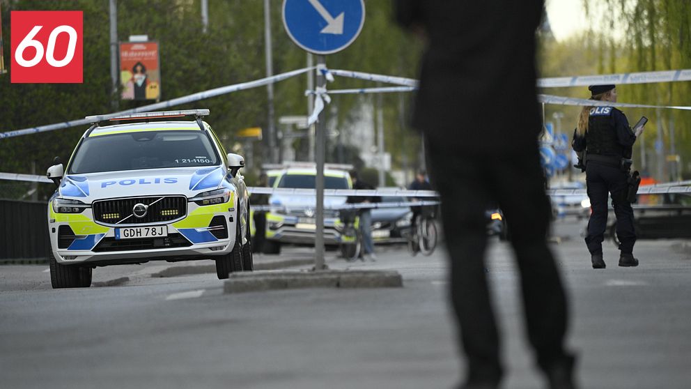 Polisbil och avspärrningar vid insats, poliser syns i bakgrunden på en avstängd gata.