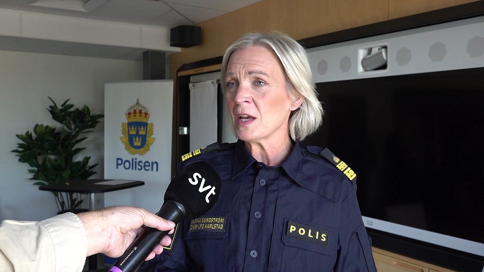 En polis med en svensk polisuniform blir intervjuad av en journalist som håller en mikrofon märkt med ”SVT”. I bakgrunden syns en växt, en TV-skärm och en skylt med Polisens logotyp.