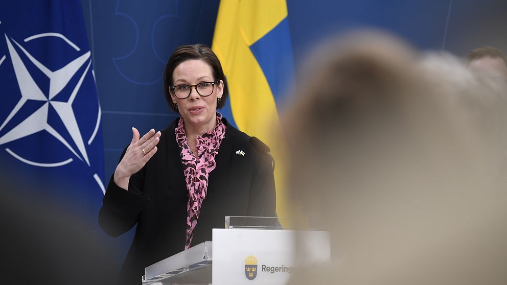 En person talar vid podiet med NATO och svenska flaggan i bakgrunden.