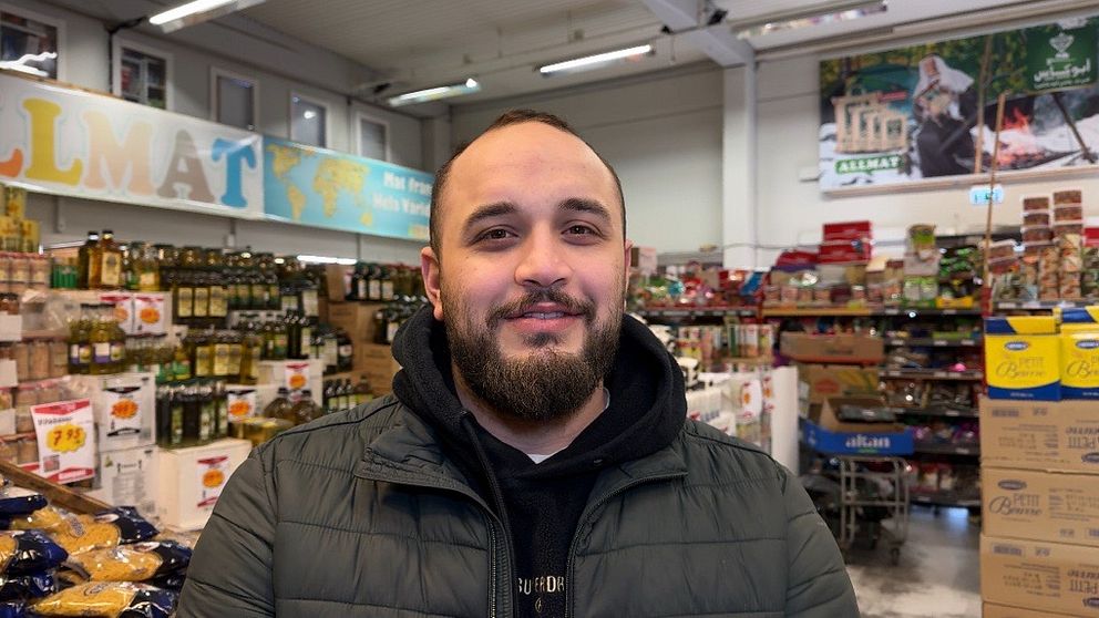 Man i grön jacka står framför hyllor i en matbutik.